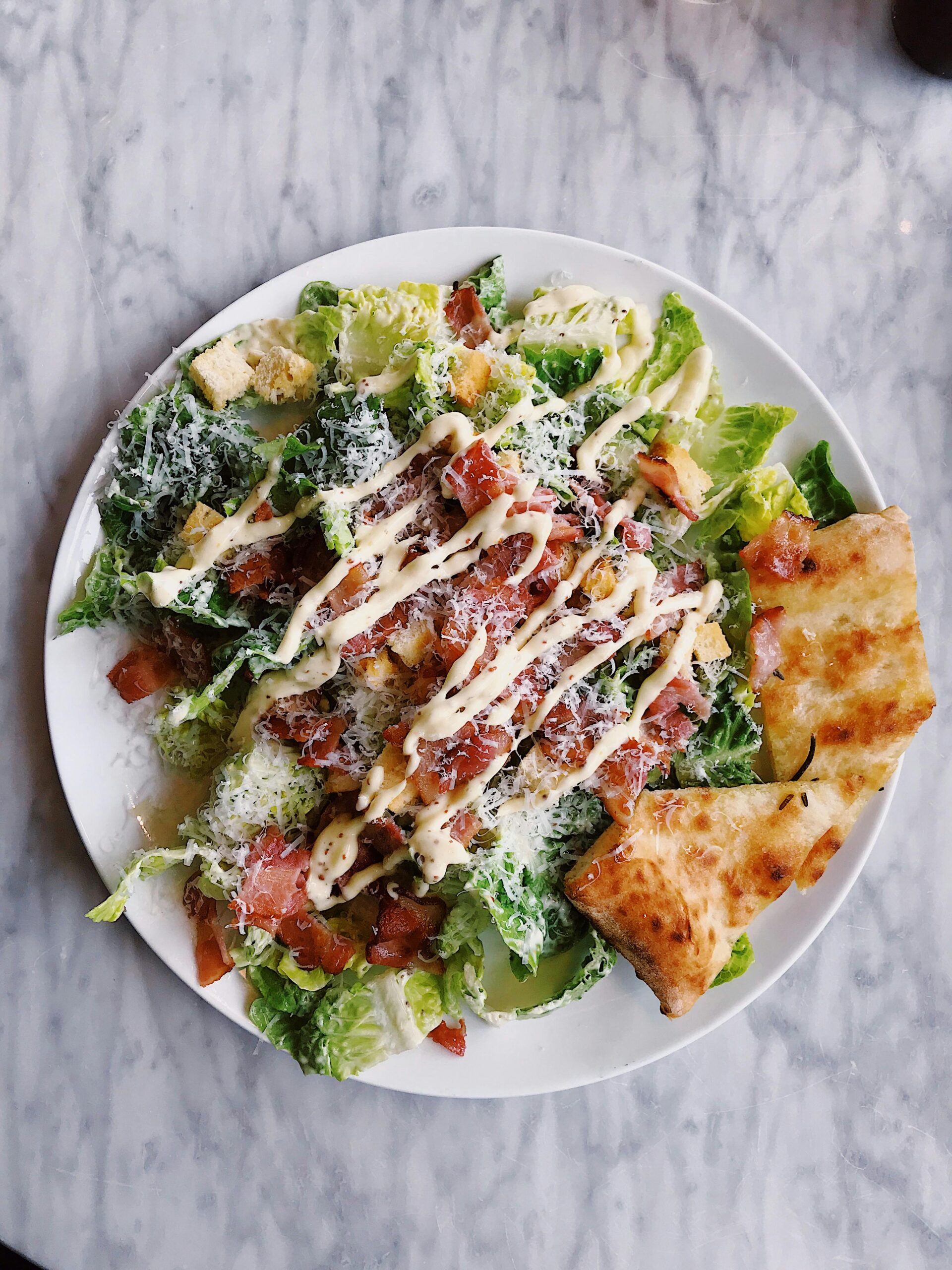 Tasty Caesar salad topped with bacon, cheese, and drizzled sauce, served with crispy bread.